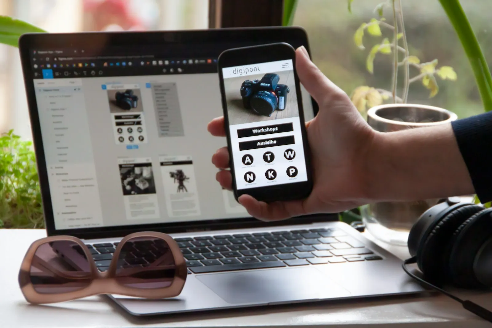 Hand holding a mug in front of a laptop showing UI design work